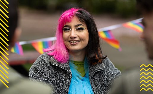 Female student with pink and black hair. Pride flags in background.